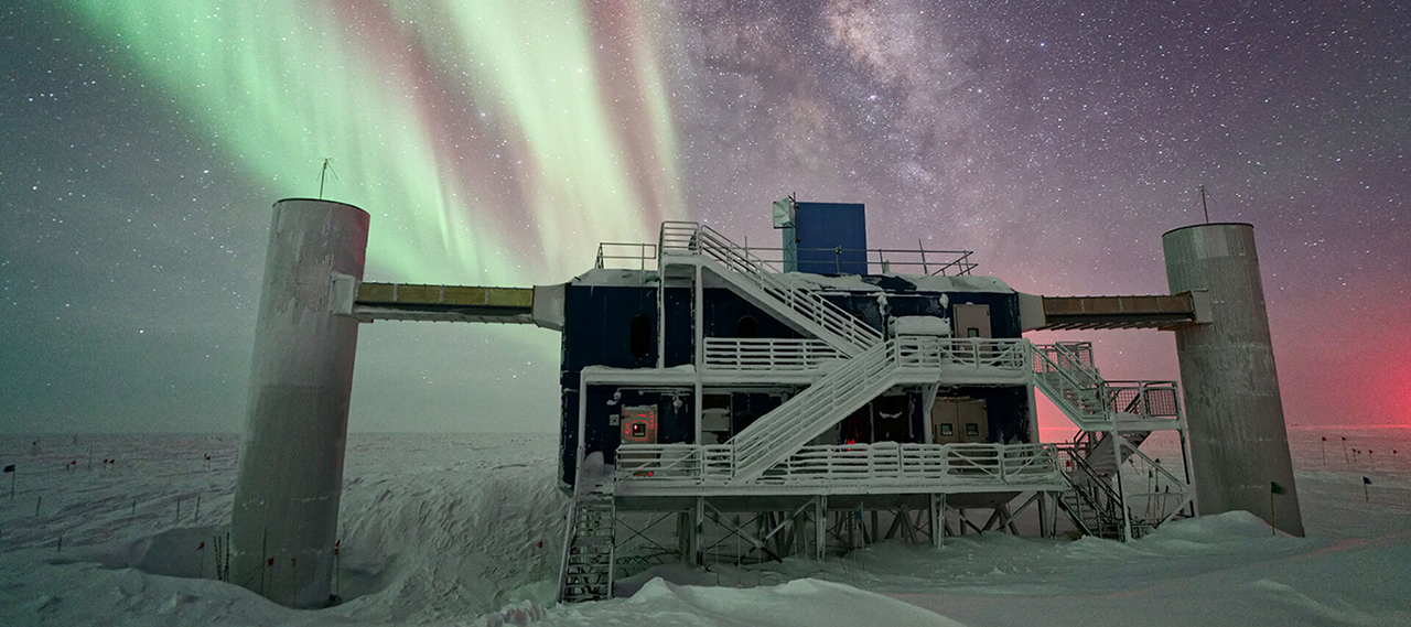IceCube Neutrino Observatory at night with the Northern Lights in the sky.
