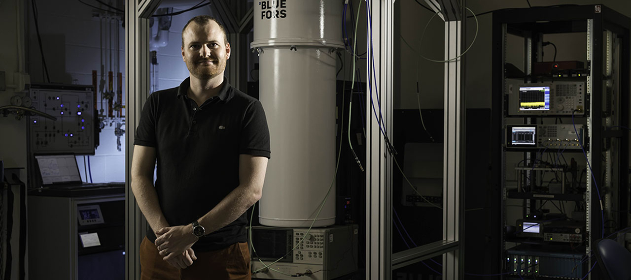 Machiel Blok, whose research builds on the fundamentals of quantum tunneling, in front of a BlueFors dilution refrigerator smiles and looks at the camera.