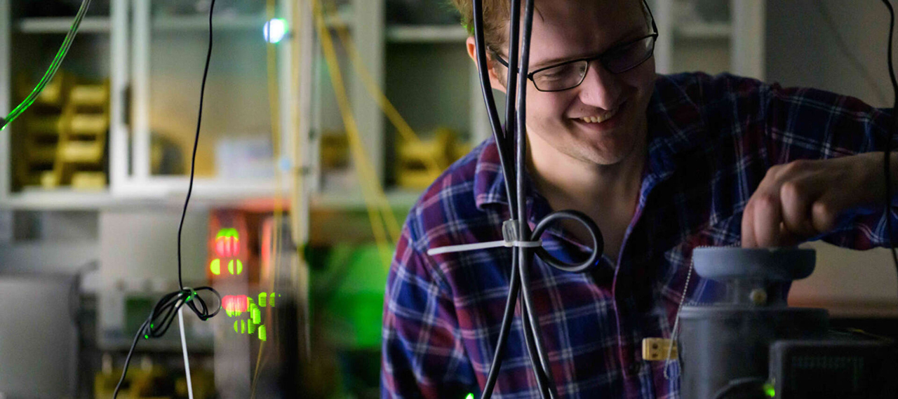University of Rochester graduate student smiles while manipulating the apparatus in an optics lab.